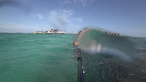 a young, fit and strong man with long hair and beard goes underwater with snorkeling goggles and then jumps back up over the surface and enjoys the sun alone by himself