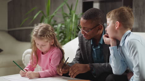 tutor and boy look at little sister writing letters at table