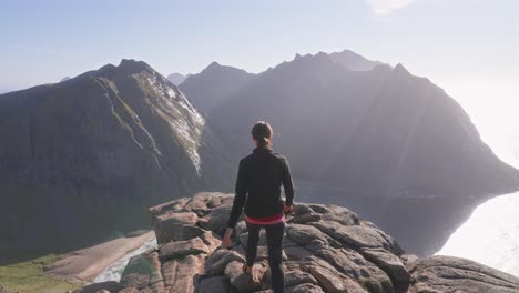 Reveal-of-a-woman-hiking-the-Peak-of-the-Kvalvika-Beach-hike-on-a-beautiful-sunny-day-in-the-Lofoten-Islands,-Norway