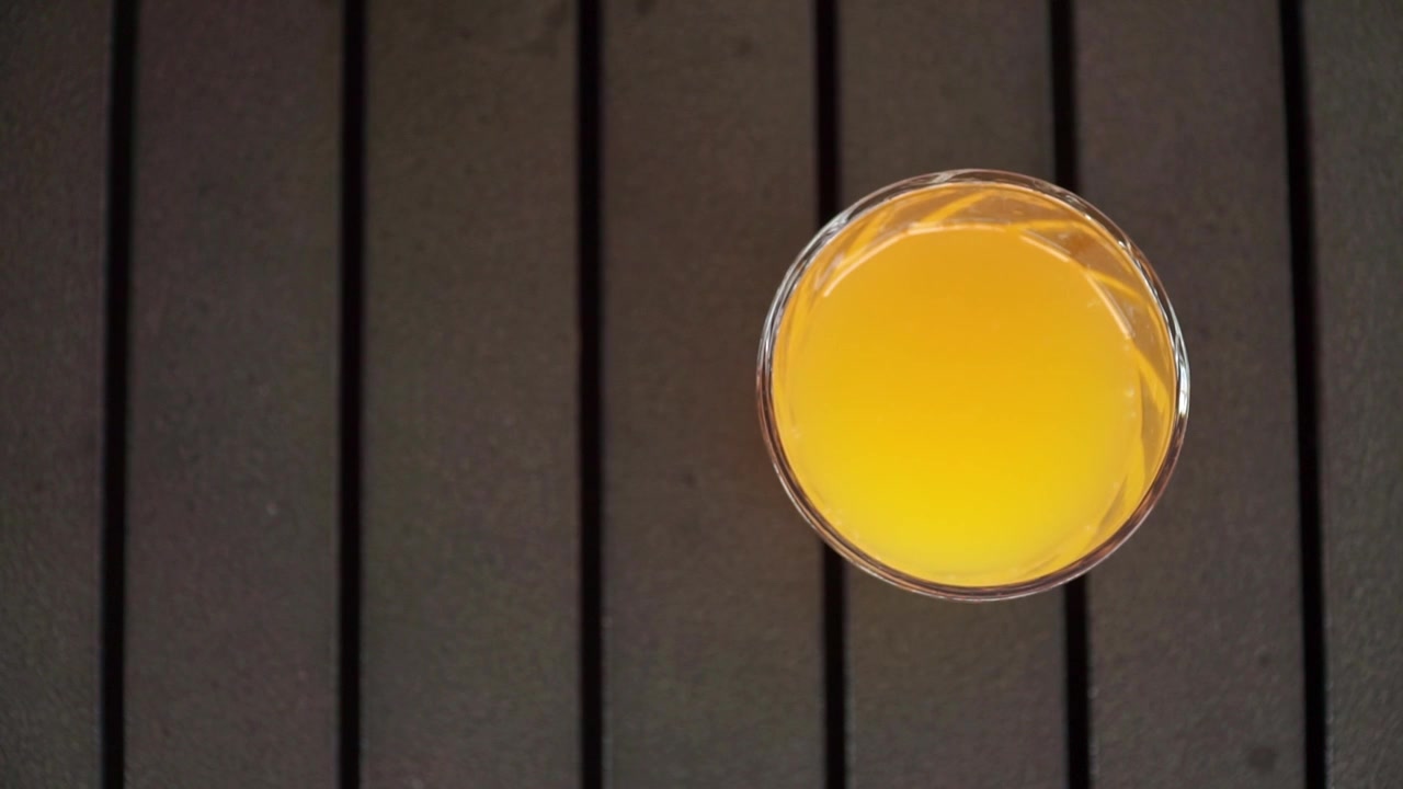 Mani che prendono un bicchiere di succo d'arancia su un tavolo nero. Adatto per riprese di colazioni, bevande salutari, bevande agli agrumi e rinfrescanti.