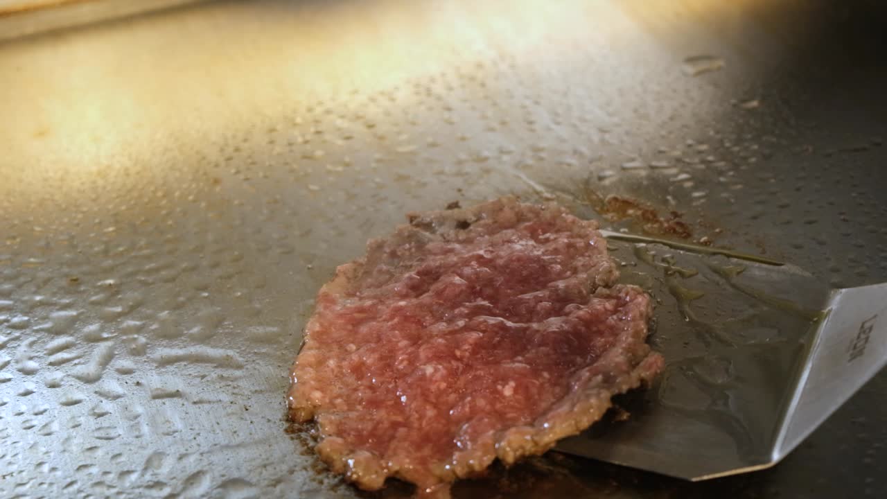 Primo piano di un hamburger di manzo capovolto su una griglia calda durante la cottura.