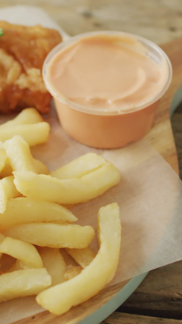 Vídeo de Peixe e Batatas Fritas em Tábua de Madeira com Molhos, Sobre Mesa de Madeira