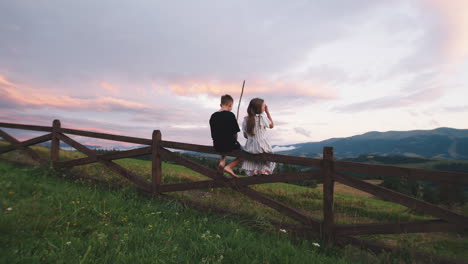 couple sitting on a fence at sunset in the mountains