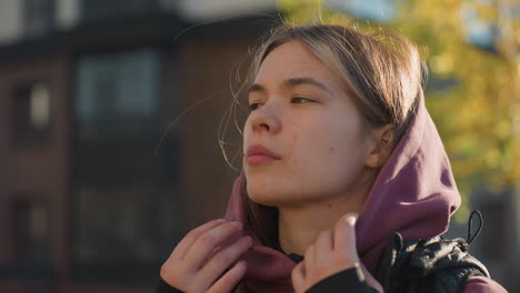 side view of casual sportswoman removing hoodie under gentle breeze brushing through hair, urban park workout setting showcasing natural movement focus energy during outdoor training session