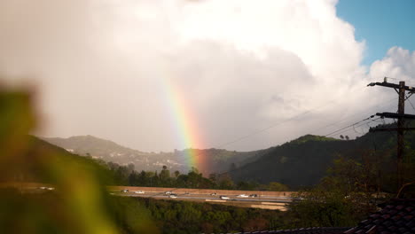 rainbow lands on freeway in green hills surrounded by clouds