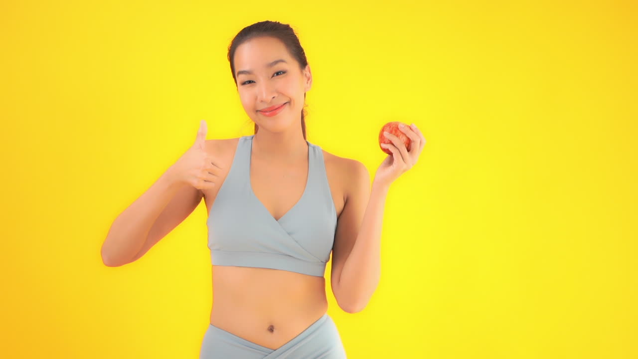 Medium shot of a young woman in workout clothes raising her hand to reveal a healthy apple snack. copy space