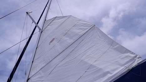 main sail is hoisted on large sailboat with metal mast in cloudy sky