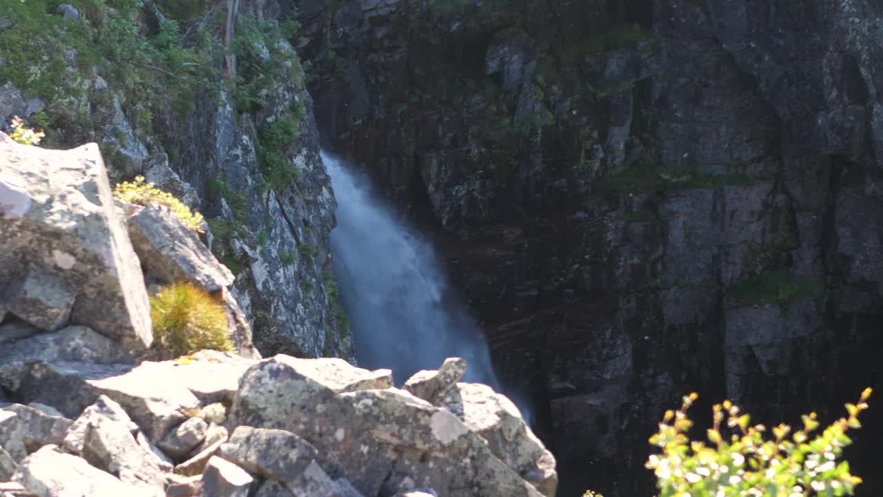 gran angular de la caída de la cascada njupeskärs, al mediodía, con mosquitos volando entre los rayos del sol, en el parque nacional fulufjället, en suecia