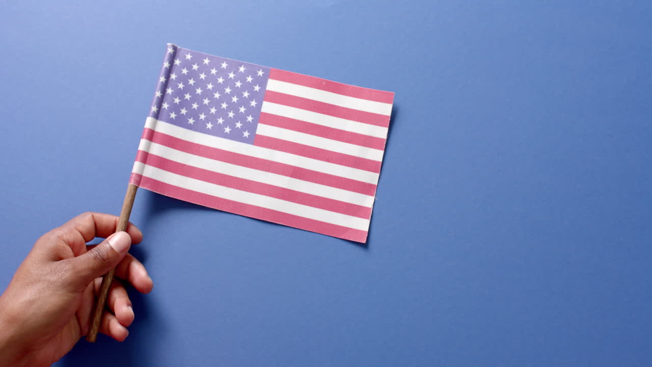 Primo piano di mano che tiene la bandiera nazionale degli Stati Uniti d'America su sfondo blu