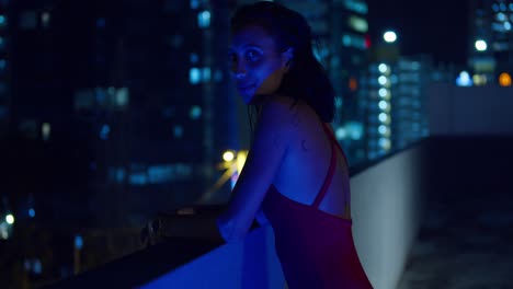 a young girl in a red dress stands on a rooftop at night, the cityscape stretching out behind her