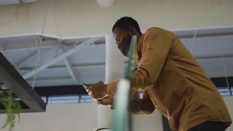 Video-Eines-Afroamerikanischen-Geschäftsmannes-Mit-Gesichtsmaske,-Der-Sein-Smartphone-Auf-Der-Treppe-Im-Büro-Benutzt