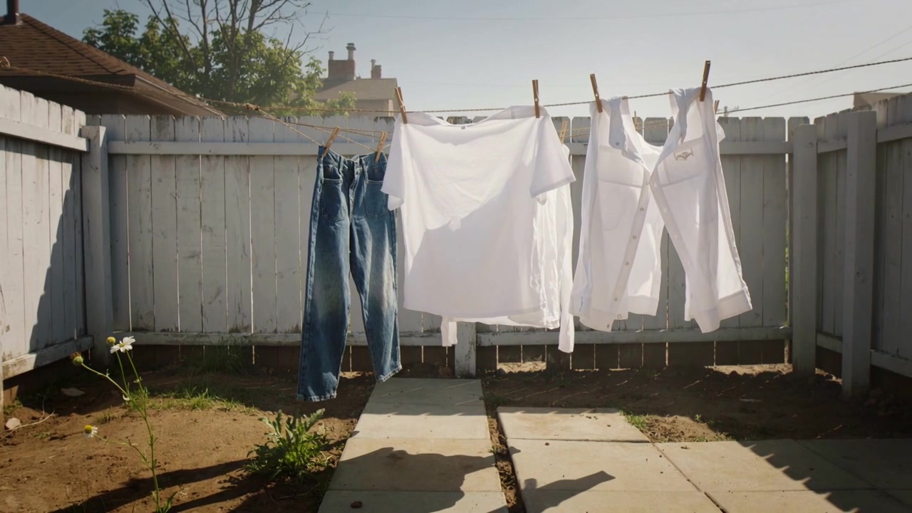 Billowing in light breeze, hanging jeans and shirts on backyard clothesline with clothespins to dry