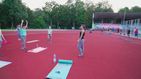 group of women doing workout on the modern stadium. young female trainer shows fitness exercises to women in the outdoor sports ground.