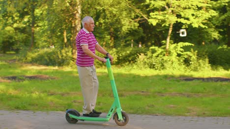 Senior-stylish-man-grandfather-riding-electric-scooter-in-park,-modern-grandpa-driving-urban-vehicle