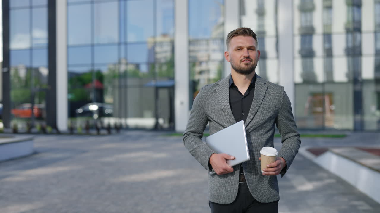 Uomo d'affari che cammina all'aperto con laptop e caffè