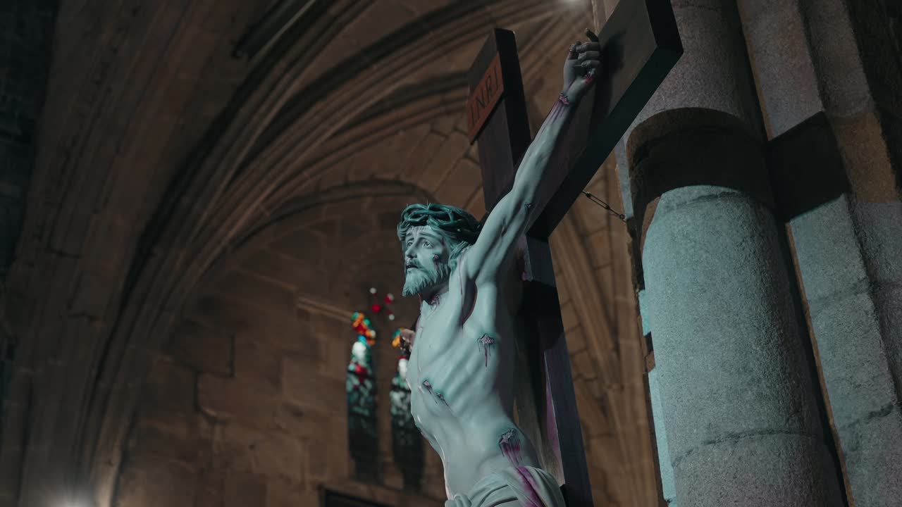 Close up of Jesus on the cross inside an old stone church with stained glass windows