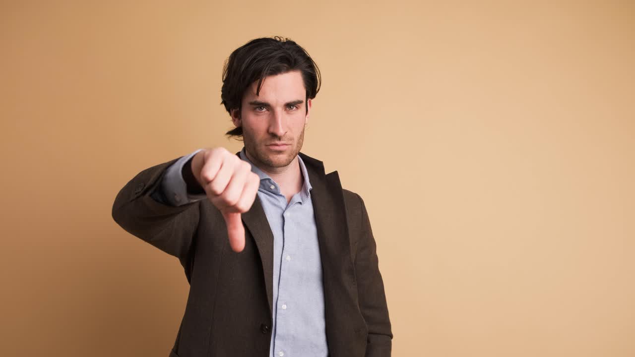 Upset businessman showing thumb down in brown studio