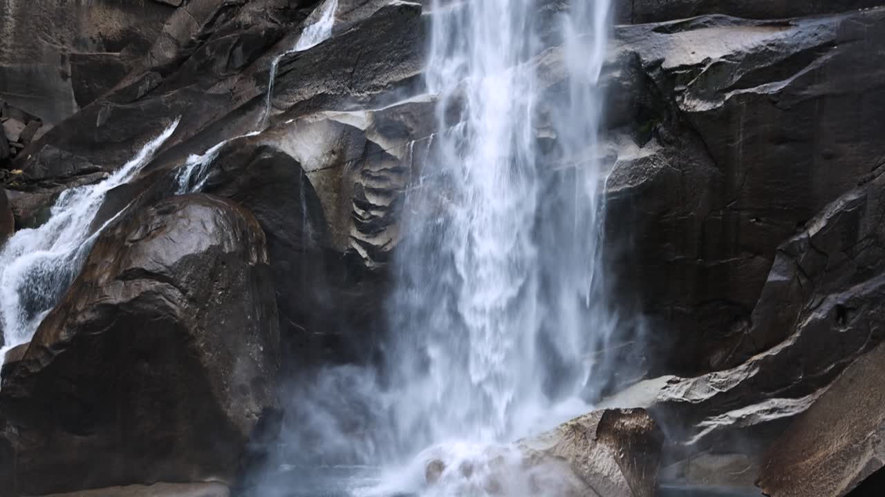 Dramatisk vårfoss nært i Yosemite nasjonalpark som slår mot steiner. Tilt opp i sakte film.