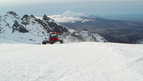 snow groomer going up mountain ploughing snow to flatten surface of ski slope