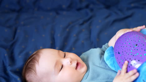 adorable baby boy lies on back having a toy in his arms. beautiful child plays with a toy and then looks into camera. top view close up.