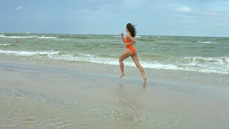 a sexy young white girl wearing swimsuit, jogging-running on the beach