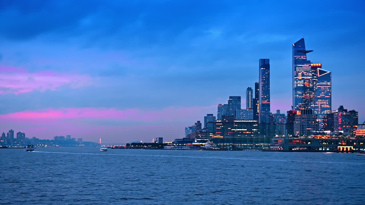 Riverboats move by the waterscape of the East River. Luminous skyline of New York, USA at sunset
