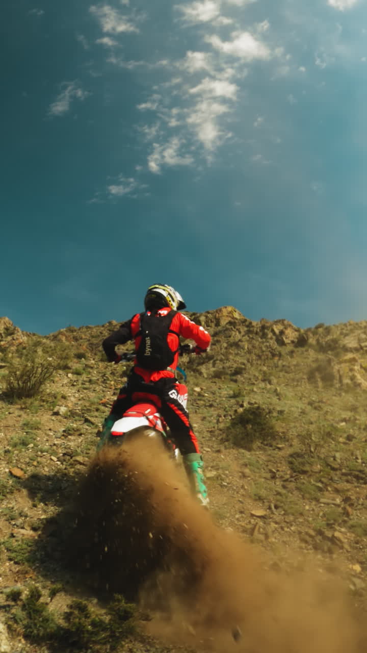 motociclista en vehículo y nube de polvo en pendiente fpv. deportista valiente en uniforme de protección monta motocicleta a lo largo de tierras montañosas. entrenamiento de deportes extremos