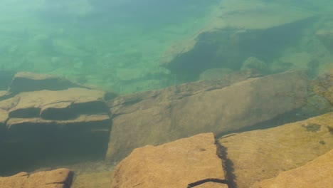 Big-cliffs-on-riverbed,-underwater-shot-of-stream-flowidng-over-rocks-in-turbid-water