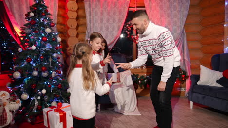 father playing rock-scissors-paper with his daughters. happy family of four are at the christmas tree. new year family celebration.