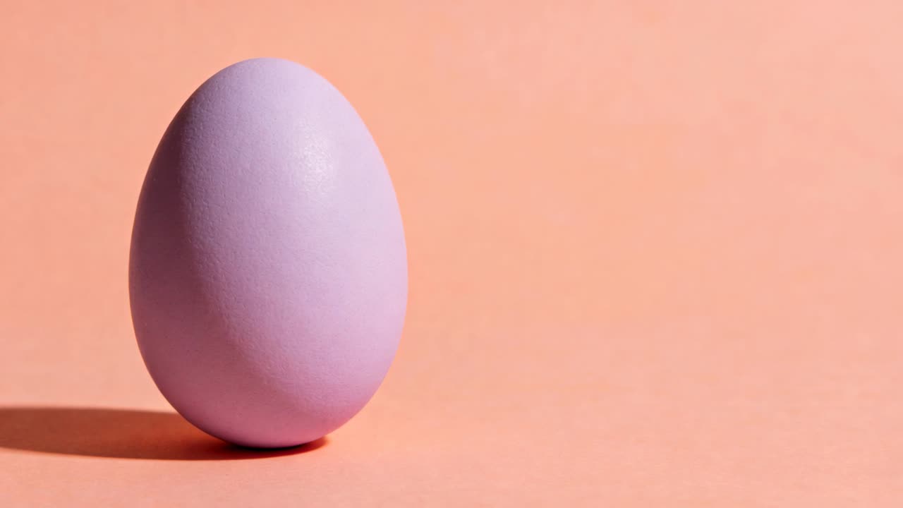 Zooming camera closing on lavender matte egg showing finish on peach backdrop shadow, copy space