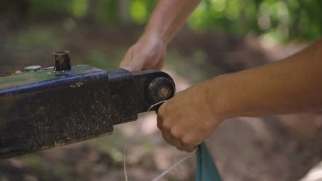 trabajador conectando equipos a un enganche de bobcat en un área boscosa de cerca.