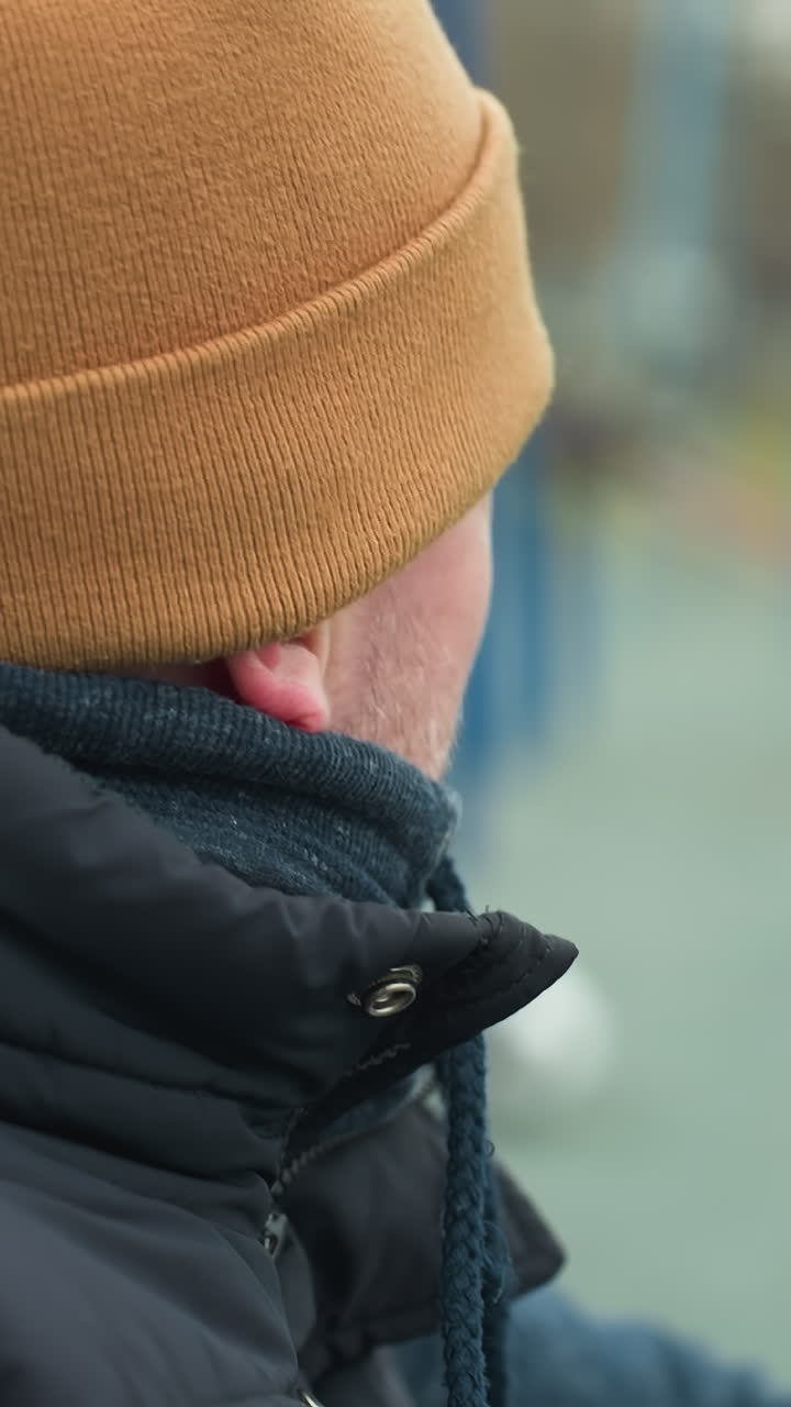 Close-up of a coach sitting on a workout equipment, looking tired as he gazes at the boys playing football in the blurred background