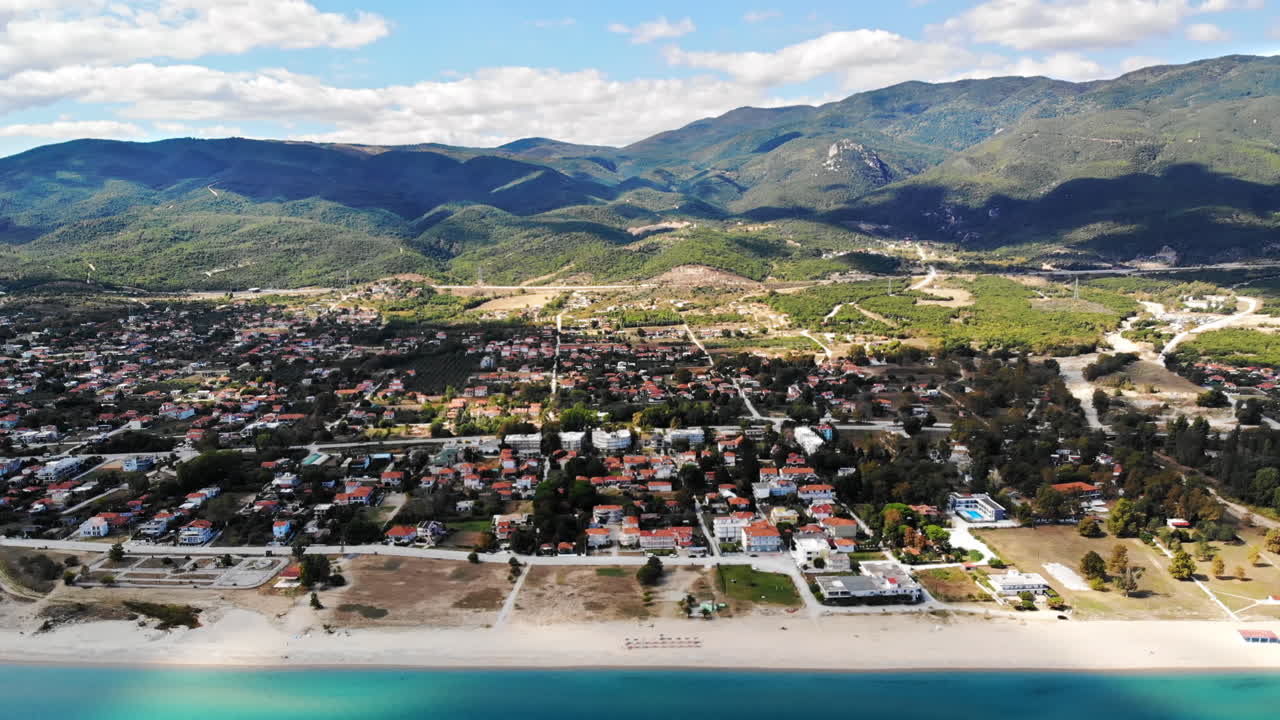 Asprovalta with multiple buildings and greenery, green hills on the background. Aegean sea coast. Long beach along the town. Sunny day. Greece