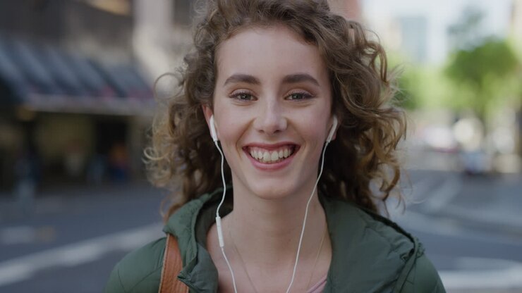 ritratto di una bella donna con la testa rossa che sorride allegra godendo di uno stile di vita urbano di successo una studentessa felice che guarda la telecamera indossando auricolari sullo sfondo della strada della città