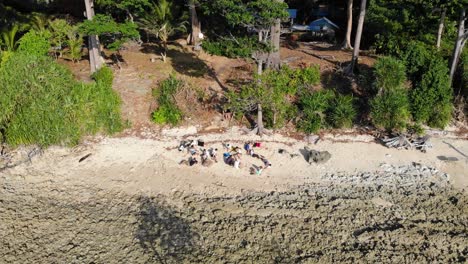 a group of individuals with rubbish bags form an sos in the sand on the beach of an andaman island as a drone flies in from the ocean at low tide over mangroves and rocks