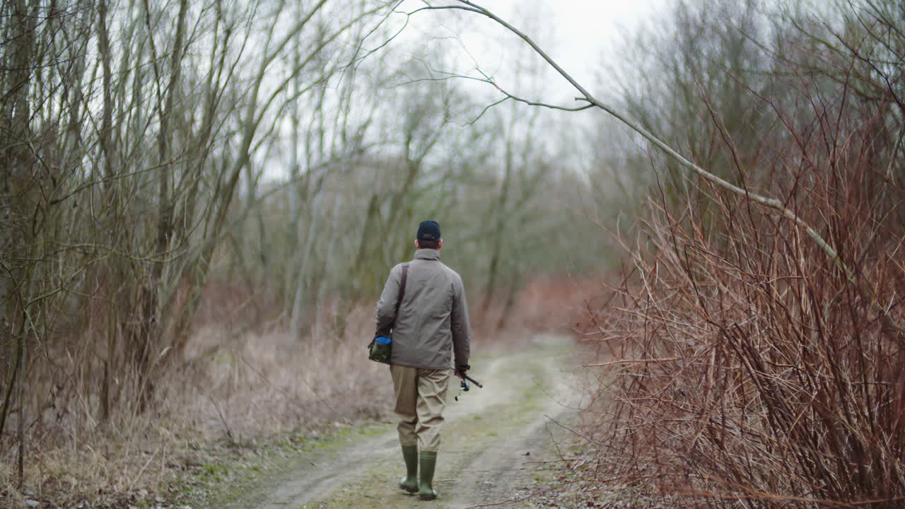 hombre con caña de pescar caminando entre árboles desnudos 5
