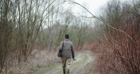 hombre con caña de pescar caminando entre árboles desnudos 5