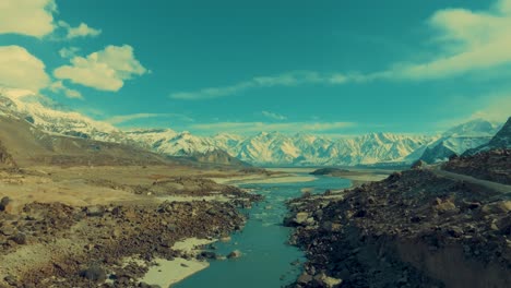 drone is flying slowly over a river in skardu with a view of a high mountain range covered in snow