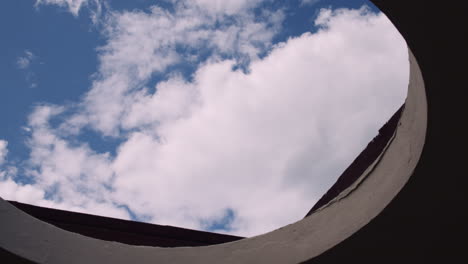 a bird gliding with spread wings against cloudy blue sky viewed from an ancient building roof with opening hole