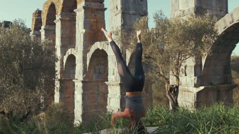 atleta femenina realizando yoga de pie en la cabeza en el antiguo acueducto