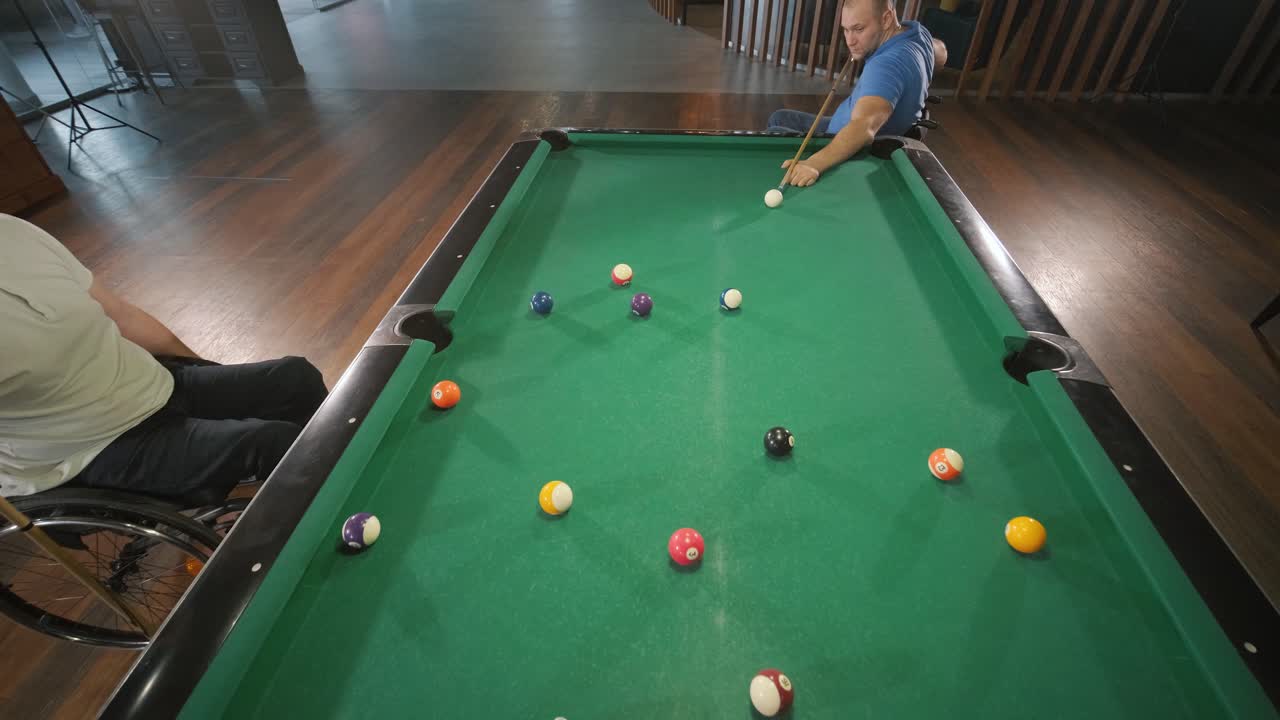 Adult men with disabilities in a wheelchair play billiards in the club