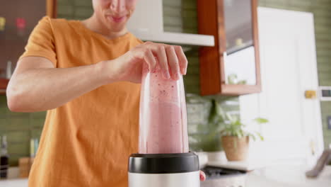 hombre biracial feliz preparando batido de frutas con licuadora en la cocina, espacio de copia, cámara lenta