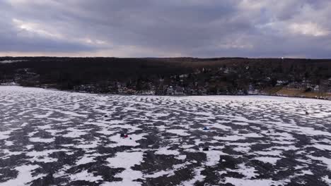 snow blowing past ice fishing tents scattered across frozen lake, aerial panoramic orbit