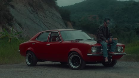 man sitting on classic red car in nature