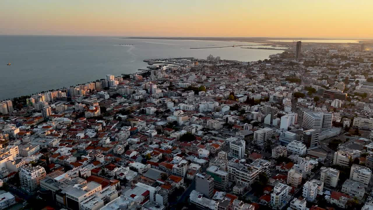 Una vista aerea cattura la vivace città di Tel Aviv al tramonto, con edifici, tetti e il mare calmo illuminati da una luce dorata. Un momento perfetto di tranquillità urbana.