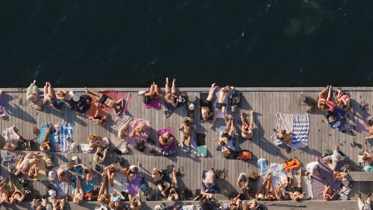 Aerial drone view of people sunbathing and swimming along the lively promenade by the harbor at the Islands Brygge waterfront