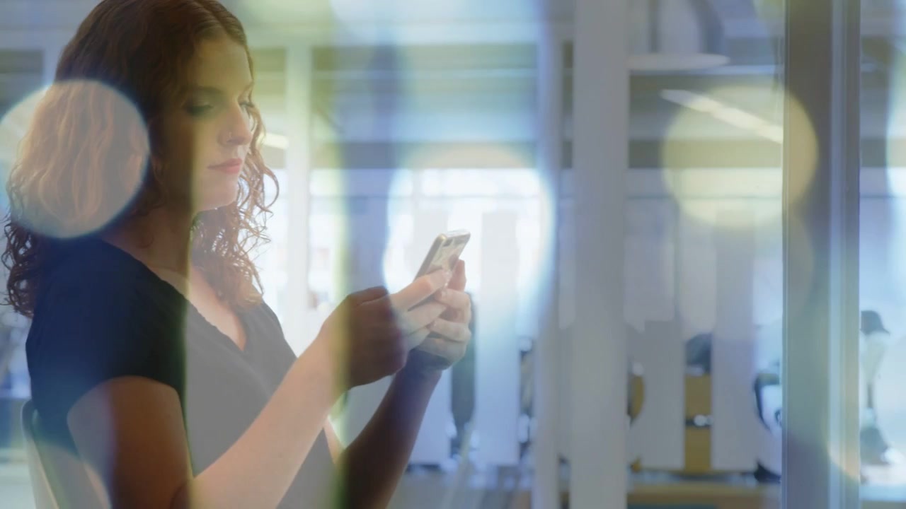 Donna in piedi accanto a una porta a vetri che tiene in mano il telefono, con una notifica animata che compare, mentre controlla i messaggi di lavoro