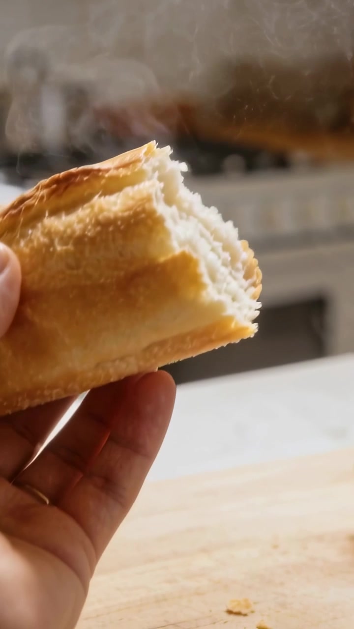 Video verticale: Mani che afferrano il pane e spezzano una baguette fumante sul bancone di casa, rivelando la mollica