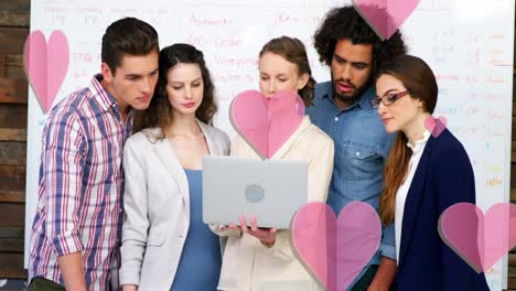 animation of pink hearts over diverse business people using laptop