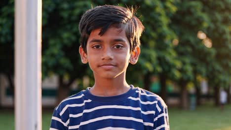 golden hour warmth enveloping young boy standing amid lush park trees, soft illumination casting gentle shadows across peaceful landscape with tranquil, contemplative expression